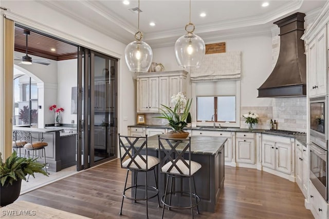 kitchen featuring a kitchen island, hanging light fixtures, stainless steel appliances, premium range hood, and a sink