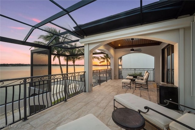 view of patio featuring glass enclosure, a water view, an outdoor hangout area, and ceiling fan