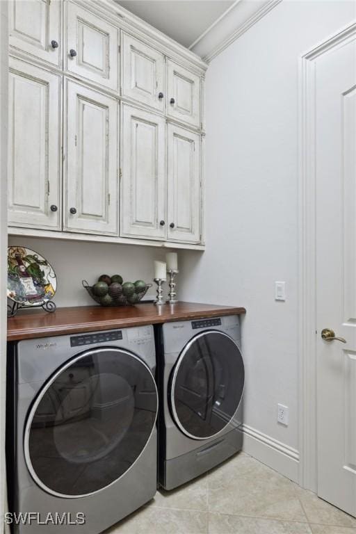 clothes washing area featuring cabinet space, baseboards, ornamental molding, washing machine and clothes dryer, and light tile patterned flooring