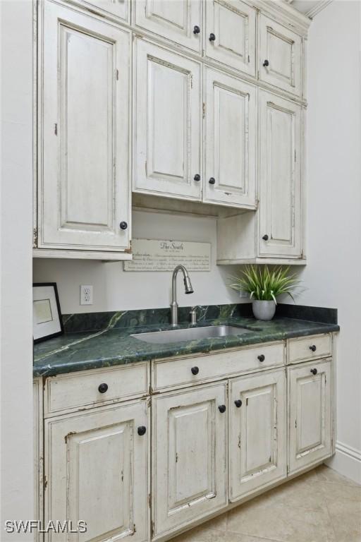 kitchen with dark countertops, baseboards, white cabinetry, and a sink