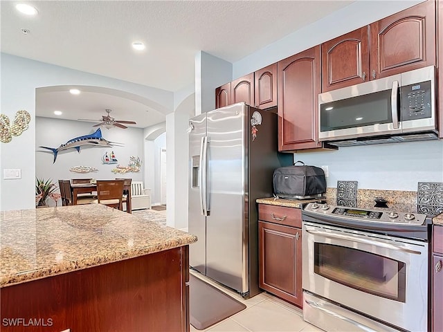 kitchen with ceiling fan, light stone counters, recessed lighting, arched walkways, and stainless steel appliances