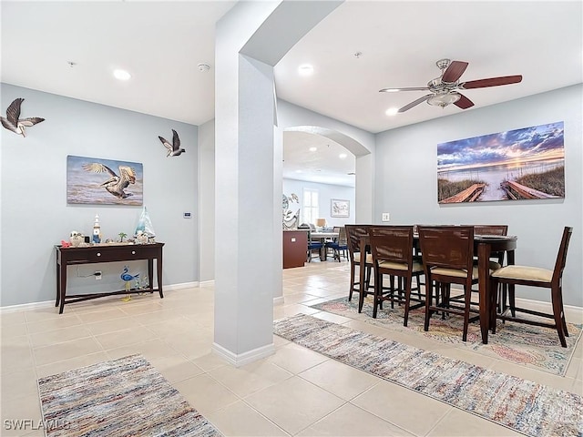 dining room featuring arched walkways, light tile patterned floors, ceiling fan, and baseboards