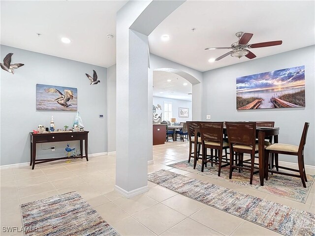 dining space with a ceiling fan, light tile patterned floors, baseboards, and arched walkways