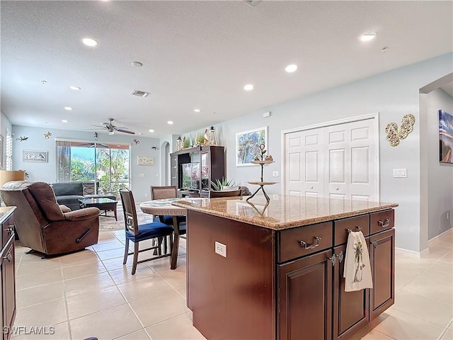 kitchen featuring light tile patterned floors, visible vents, dark brown cabinets, and open floor plan