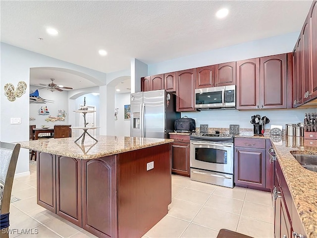 kitchen with light stone counters, light tile patterned floors, a kitchen island, ceiling fan, and stainless steel appliances