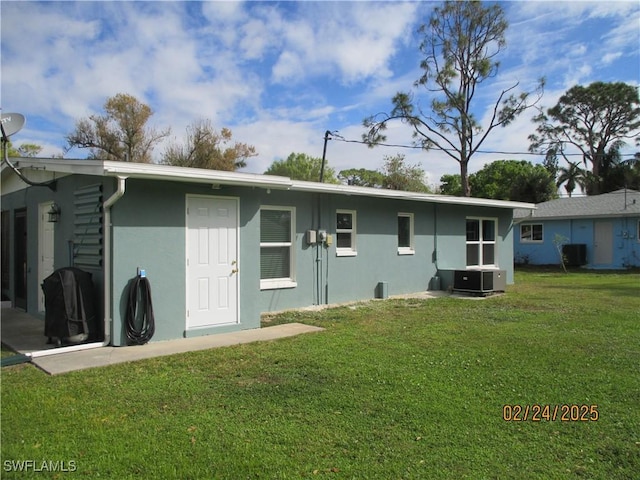 rear view of property with central air condition unit, a yard, and stucco siding