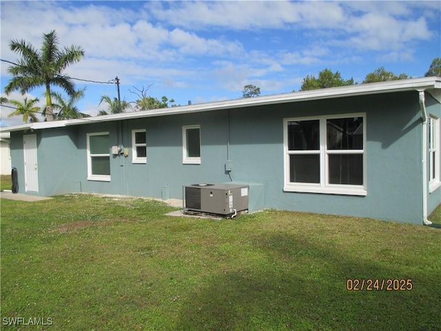 rear view of property featuring central AC, a lawn, and stucco siding