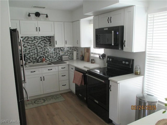 kitchen featuring tasteful backsplash, visible vents, white cabinetry, a sink, and black appliances