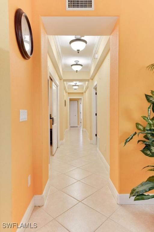 hallway featuring visible vents, ornamental molding, baseboards, and light tile patterned flooring