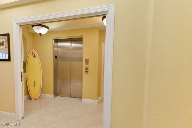 hall featuring elevator, light tile patterned flooring, and baseboards