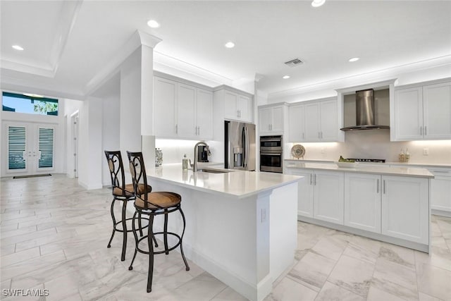 kitchen featuring visible vents, appliances with stainless steel finishes, a sink, a peninsula, and wall chimney exhaust hood