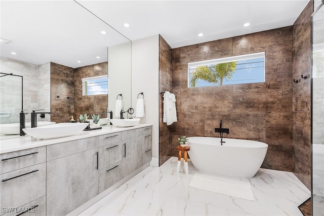 bathroom with tile walls, a freestanding tub, a sink, and marble finish floor