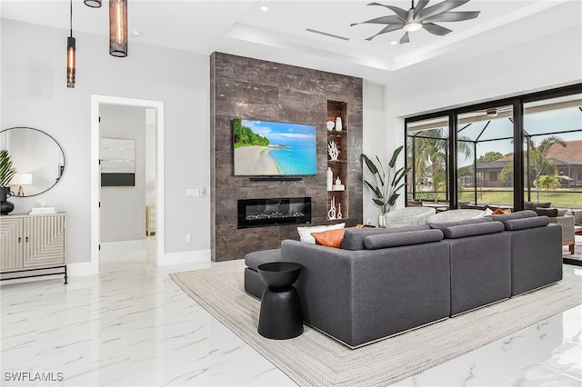 living area with a tray ceiling, marble finish floor, a ceiling fan, a tile fireplace, and baseboards