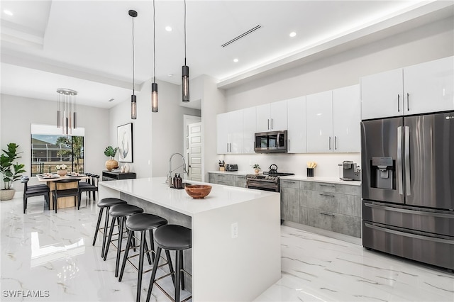 kitchen featuring marble finish floor, stainless steel appliances, light countertops, hanging light fixtures, and a kitchen island with sink