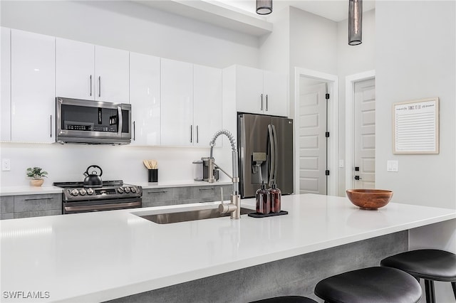 kitchen with appliances with stainless steel finishes, white cabinets, light countertops, and a kitchen bar