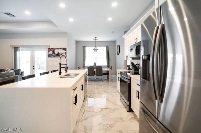 kitchen with a center island with sink, appliances with stainless steel finishes, light countertops, white cabinetry, and a sink