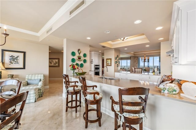 kitchen with crown molding, a raised ceiling, visible vents, white cabinetry, and a sink