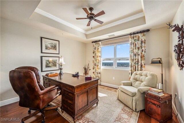 office featuring wood finished floors, a ceiling fan, baseboards, a raised ceiling, and crown molding