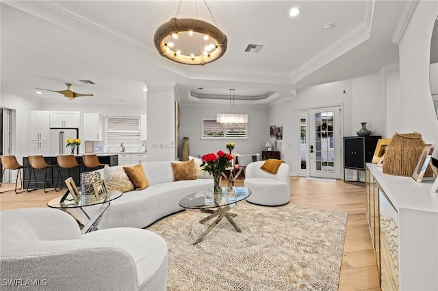 living room featuring visible vents, a tray ceiling, a notable chandelier, and ornamental molding