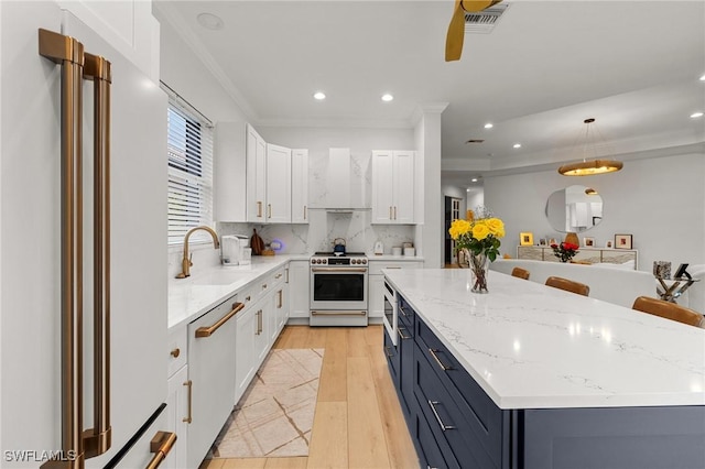 kitchen featuring stainless steel appliances, a sink, white cabinetry, wall chimney exhaust hood, and pendant lighting