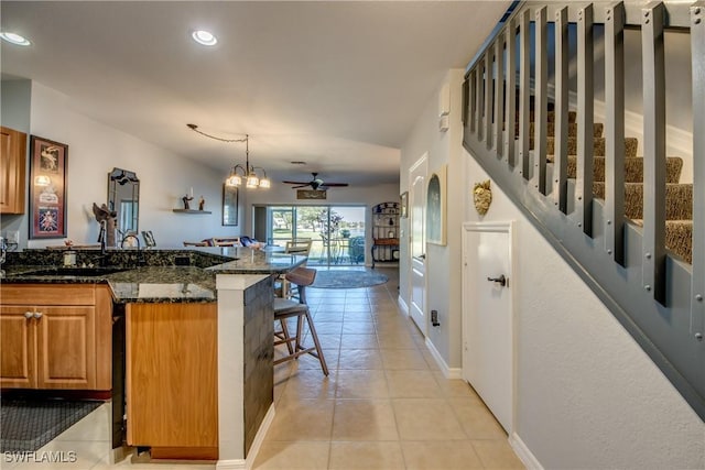 kitchen featuring light tile patterned floors, dark stone counters, a breakfast bar area, brown cabinets, and pendant lighting