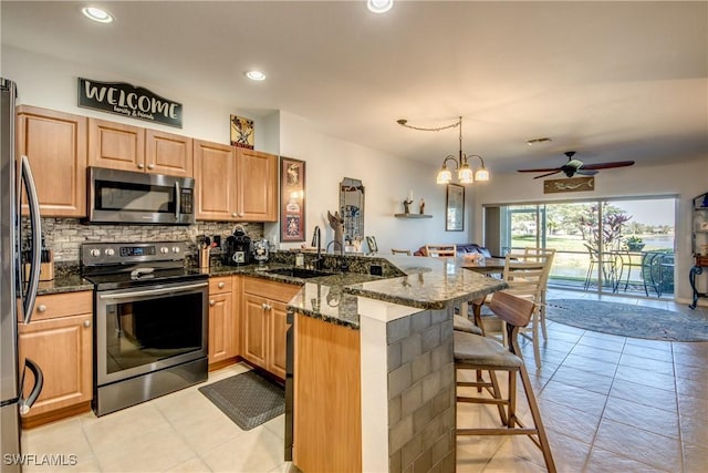 kitchen with appliances with stainless steel finishes, a sink, dark stone counters, a peninsula, and a kitchen breakfast bar