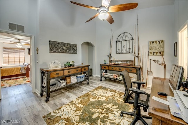 office area with arched walkways, visible vents, a high ceiling, and wood finished floors