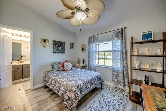 bedroom featuring light wood-style floors, lofted ceiling, baseboards, and ensuite bathroom