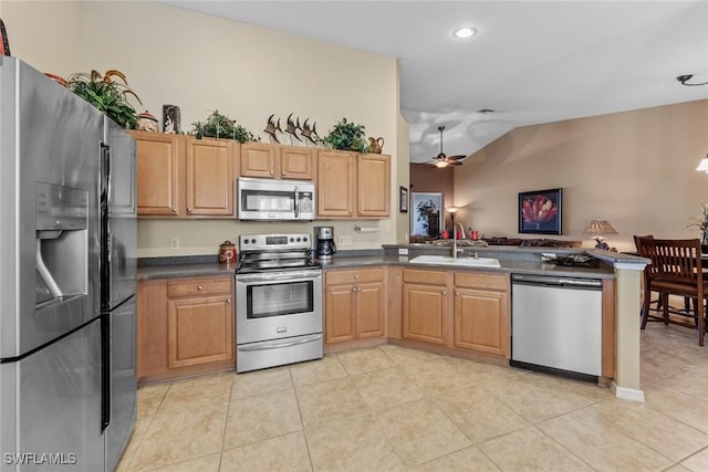 kitchen with stainless steel appliances, dark countertops, a ceiling fan, a sink, and a peninsula