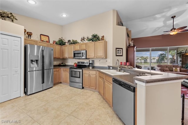 kitchen with a peninsula, appliances with stainless steel finishes, dark countertops, and a sink