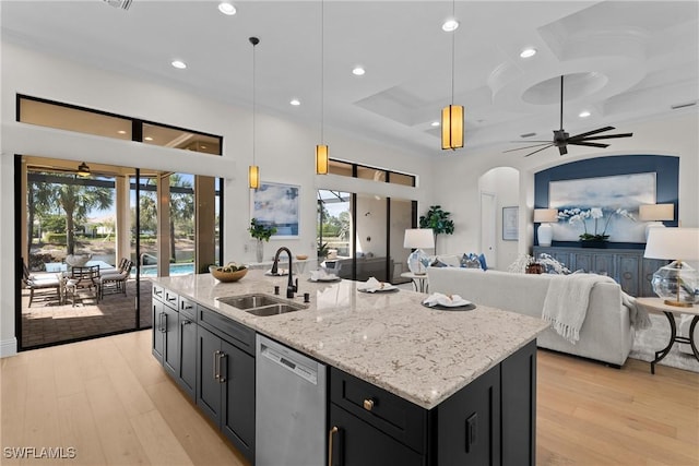 kitchen featuring arched walkways, light wood-style floors, a sink, dark cabinetry, and dishwasher