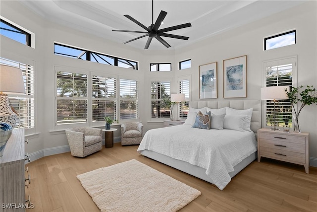 bedroom with a tray ceiling, ceiling fan, light wood-style flooring, and baseboards