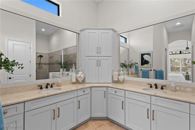 ensuite bathroom featuring double vanity, a sink, and tiled shower