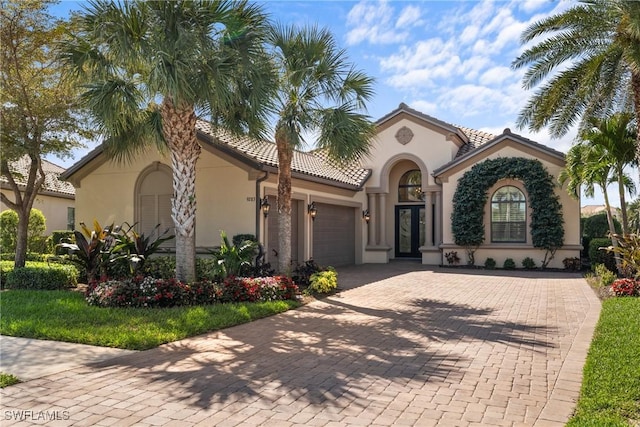 mediterranean / spanish house with a garage, a tile roof, decorative driveway, and stucco siding