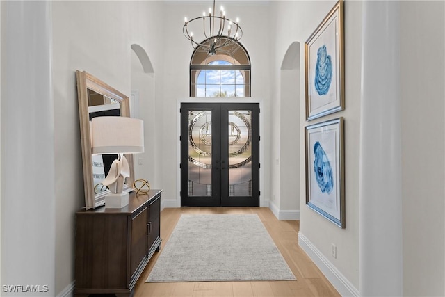 foyer entrance featuring baseboards, french doors, arched walkways, and a notable chandelier