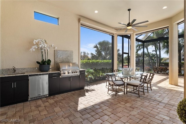 view of patio featuring ceiling fan, glass enclosure, an outdoor kitchen, area for grilling, and a sink