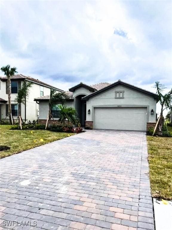 view of front of property featuring a garage, decorative driveway, a front lawn, and stucco siding