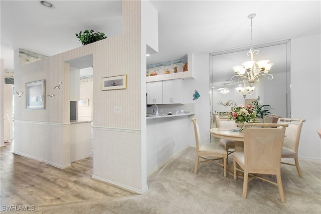 dining area with a notable chandelier, light carpet, baseboards, light wood-type flooring, and wallpapered walls