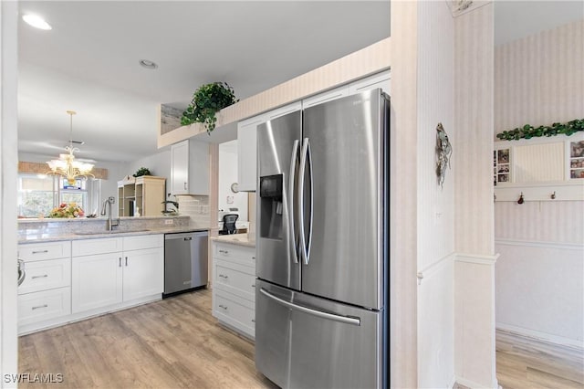 kitchen with light stone counters, light wood finished floors, appliances with stainless steel finishes, white cabinets, and a sink