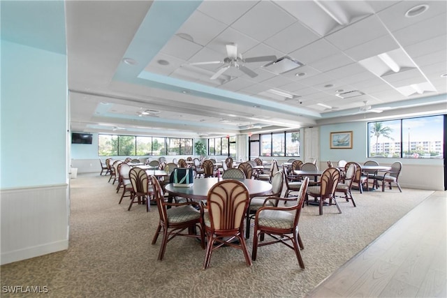 dining space with ceiling fan, a wainscoted wall, and a healthy amount of sunlight