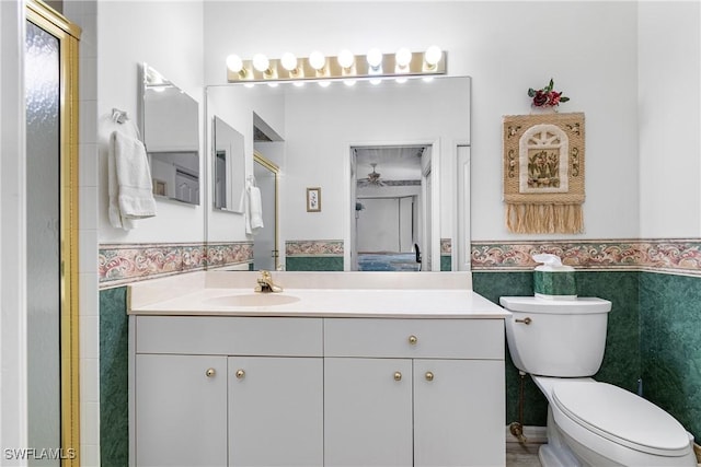 bathroom with wainscoting, toilet, an enclosed shower, vanity, and tile walls