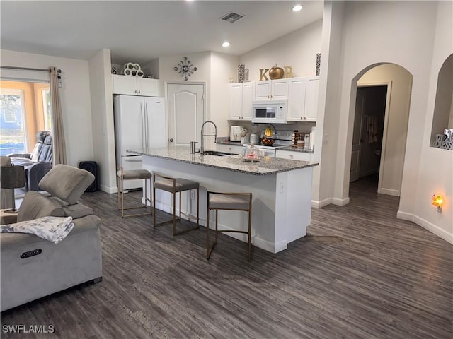 kitchen featuring a breakfast bar, arched walkways, a kitchen island with sink, white cabinetry, and white appliances