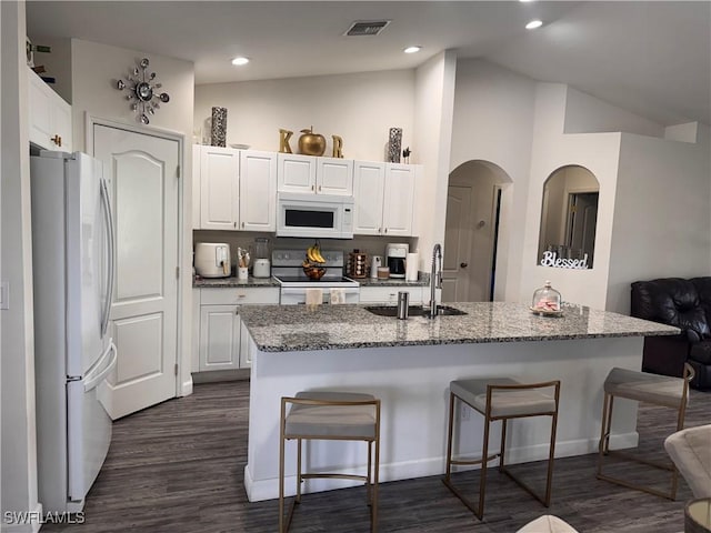 kitchen featuring stone counters, a breakfast bar, white cabinetry, a sink, and white appliances