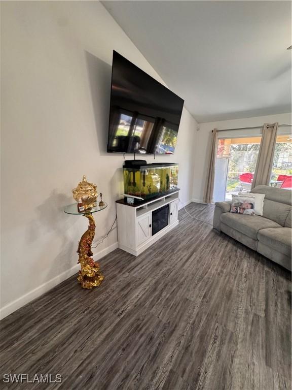 unfurnished living room featuring lofted ceiling, dark wood-style flooring, and baseboards