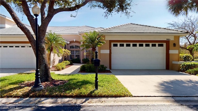 view of front of property with stucco siding, a front yard, a garage, driveway, and a tiled roof