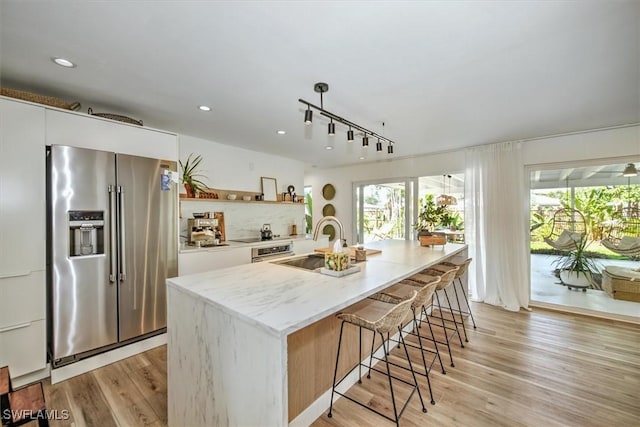 kitchen featuring open shelves, high end refrigerator, a center island with sink, and white cabinets