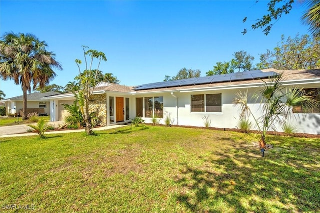 ranch-style home featuring driveway, stucco siding, an attached garage, roof mounted solar panels, and a front yard