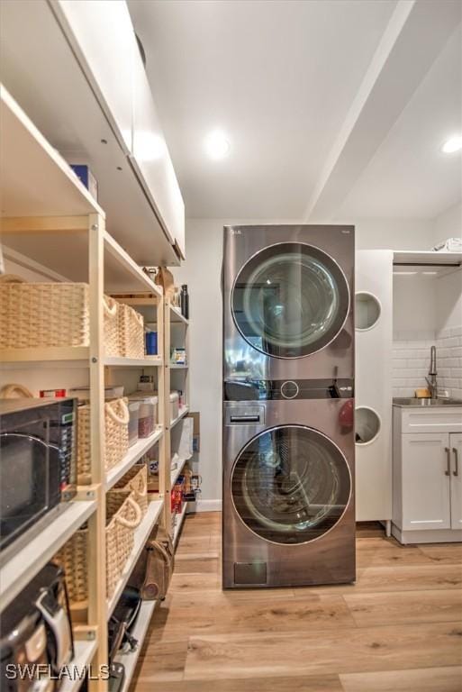 clothes washing area featuring laundry area, light wood-style flooring, stacked washing maching and dryer, a sink, and recessed lighting