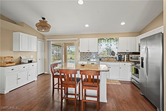 kitchen with lofted ceiling, appliances with stainless steel finishes, a kitchen island, and white cabinetry