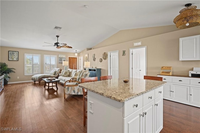 kitchen with light stone counters, a kitchen island, white cabinets, open floor plan, and vaulted ceiling